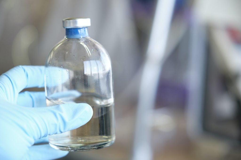 Researcher hand wearing gloves holding a bottle for anaerobic cultures, with cap and septum